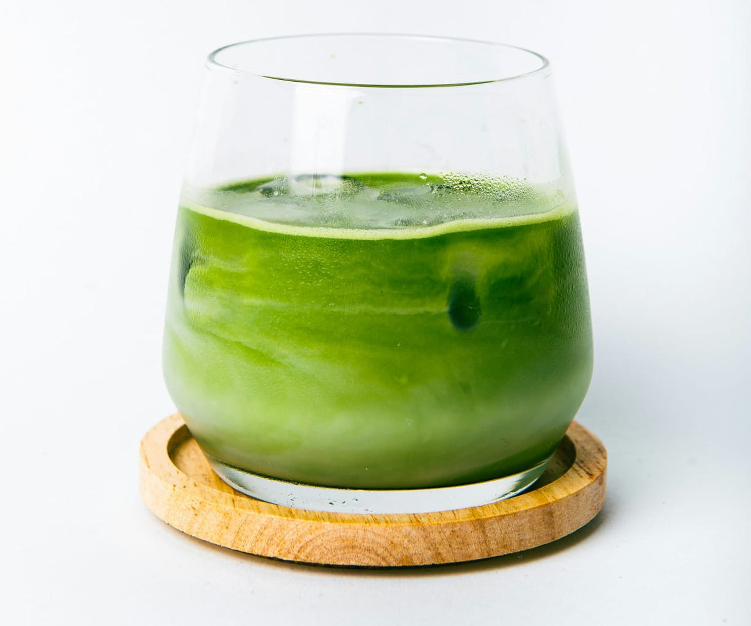 Green smoothie in a glass on a wooden coaster with a white background