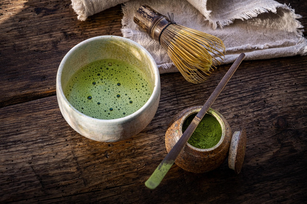 Ceramic bowl with green tea, whisk, and small container on a wooden surface